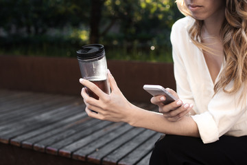 Young attractive woman at park, working with phone, drinking coffee, having lunch in a hurry. Business concept photo