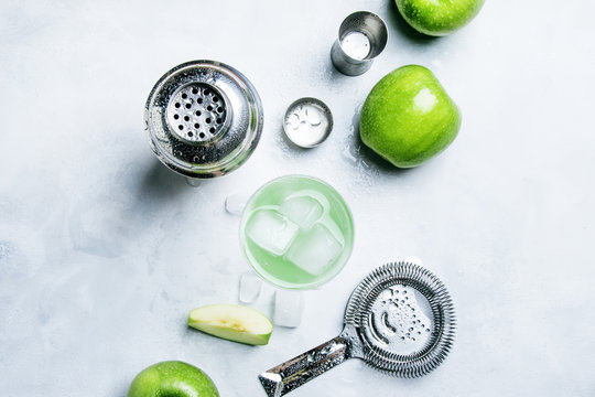 Summer alcoholic cocktail with green apple, vermouth and ice, bar tools, gray background, top view