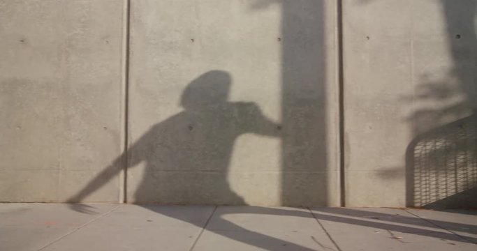 Shadow of hip hop man freestyle dancing down city sidewalk 