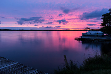 Colorful pink, purple & blue sunset over a calm lake with a pontoon boat at the shore. Beautiful...