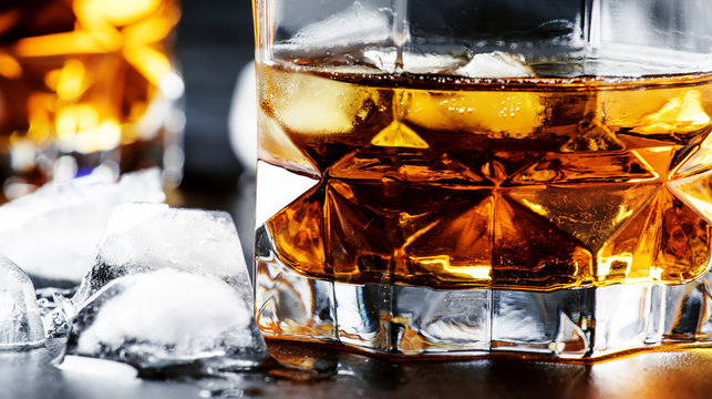 Cold whiskey with ice cubes in black table, selective focus