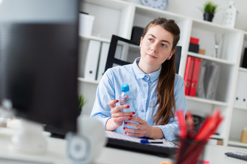 A young girl sits at a table in the office and holds a bottle of water in her hand.