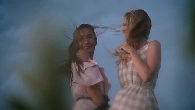 Two young charming girls in dresses is enjoing wind and laughing in field in rainy day in summer, freedom concept, bottom view