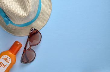 Summer concept, a set of hat, sunglasses, cream against sunburn on a blue background top view