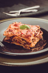 Traditional Italian Lasagna With Minced Beef, Tomato Sauce and Green Basil on Dark Plate