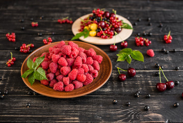 Raspberry, cherry, red currant, blackcurrant on a wooden plate against a dark background. It can be used as a background
