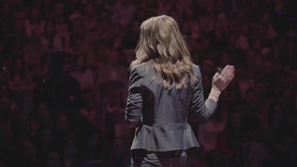 Expert perform on the stage address to modern crowd audience sitting and listening in large hall. Female entrepreneur communicating with a listener at workshop convention for young businesspersons