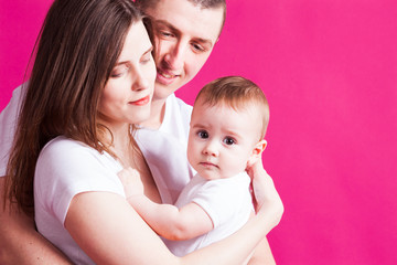 Beautiful family is posing with their infant, pink background