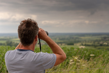 man in striped T shirt with beard looking at distant scenery with binoculars