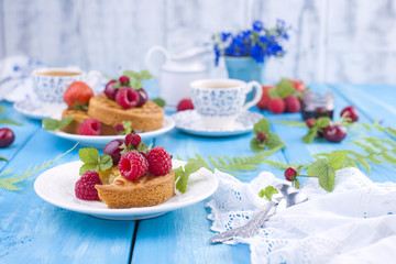 Delicious summer breakfast, homemade pastries and fragrant coffee. On a blue wooden background, berries and green leaves and flowers. Copy space