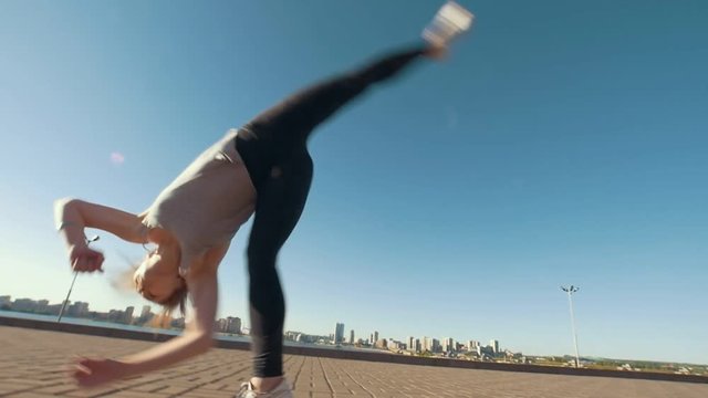 Young caucasian woman performs acrobatic flip on the asphalt on background cityscape
