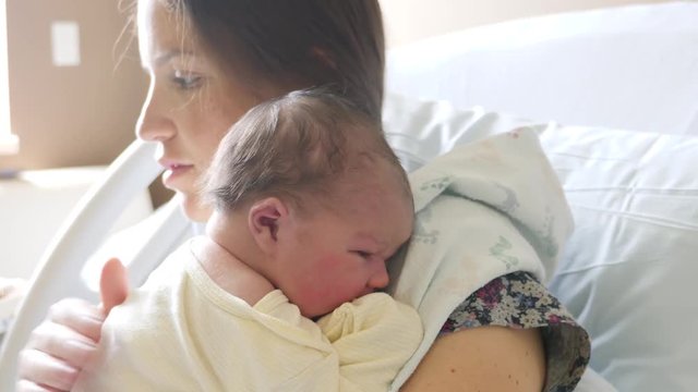 Tired mother burping a newborn girl after nursing in the hospital