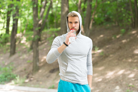 Sport and healthy lifestyle concept. Man with athletic appearance holds bottle with water. Man athlete in sport clothes training outdoor. Athlete drinks water after training, nature background