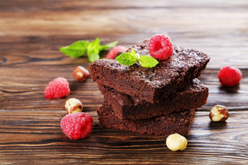 Square pieces of homemade brownies with dark chocolate spread paste, hazelnut & raspberry on wood...