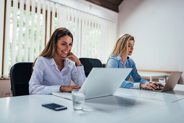 Two businesswoman working on laptop computers side by side.