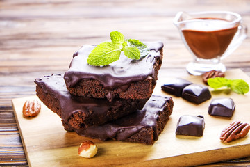 Square slices of homemade brownies with dark chocolate spread paste, pecan nut, hazelnut on wood texture table. High calorie pastry. Cocoa based sweets, bad for figure. Close up, background, top view.