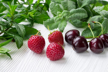 Red cherries, strawberries, fresh mint and melissa on white wood