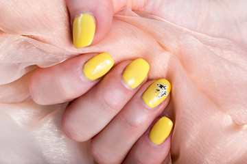 Female with yellow nails manicure polish holding soft pink silk fabric. Woman beauty concept. Close up, selective focus