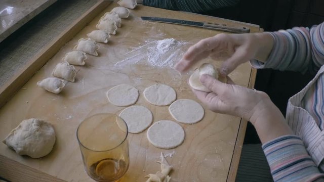 woman hand shaping traditional Polish dumplings , pierogi. They contain white cottage cheese with onions and mashed potatoes  . full proccess.