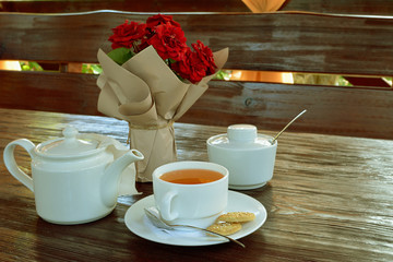 Still life from a bouquet of scarlet roses, a white teapot and a mug of tea.