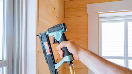 Carpenter brad using nail gun to moldings on framing trim, close up on hand and nail gun