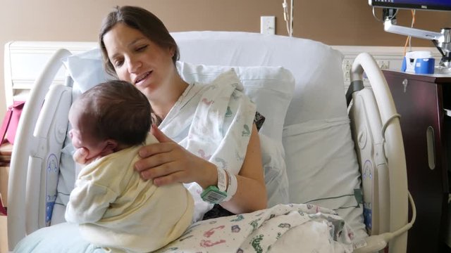 Tired mother burping newborn girl after nursing in the hospital