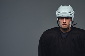 Hockey player wearing black protective gear and white helmet holds a hockey stick on a gray background.