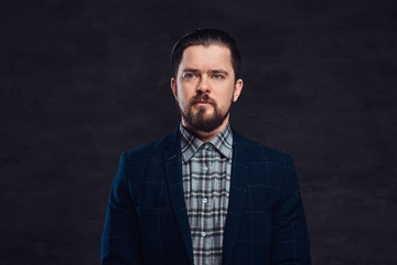 Close-up portrait of a middle-aged man with beard and hairstyle dressed in an elegant blue suit. Isolated on a textured dark background in studio.