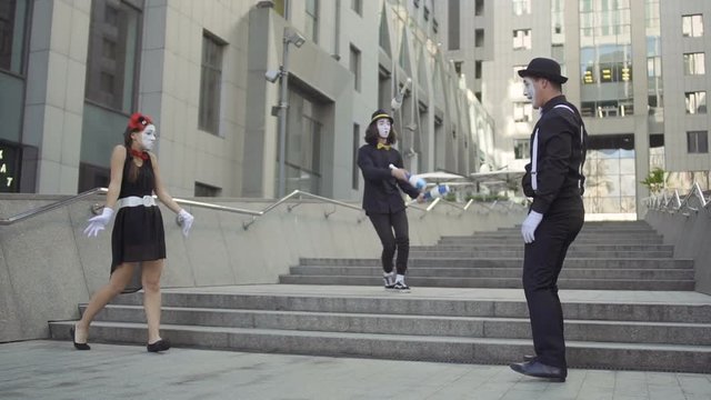 Company of three mimes have fun standing near office center background
