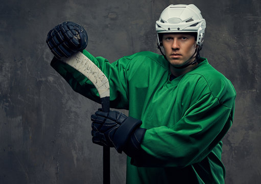 Hockey Player Wearing Green Protective Gear And White Helmet Standing With The Hockey Stick. Isolated On A Gray Background. 