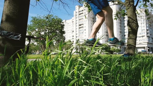 Young man slowly steps along the lines in the city park. Guy balances on slackline, slow motion