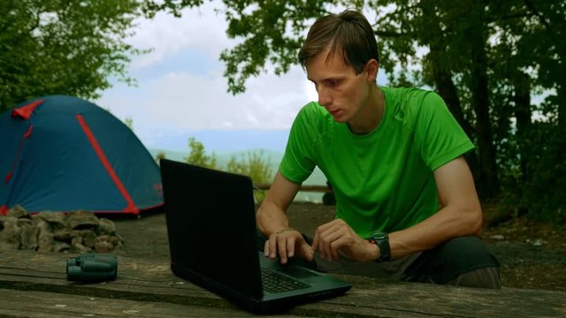 Businessman working on a laptop in a forest, free space. Working on vacation, freelancing.