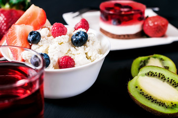 Cottage cheese with strawberries, blueberries and raspberries in white plate with kiwi, freshly squeezed juice and cake, proper nutrition