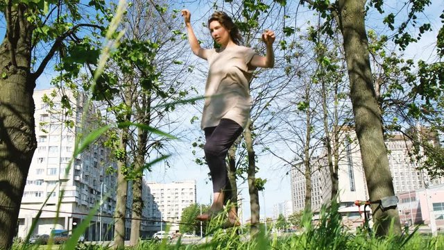 Young beautiful girl is walking along a tight line in a city park. Woman balances on slackline