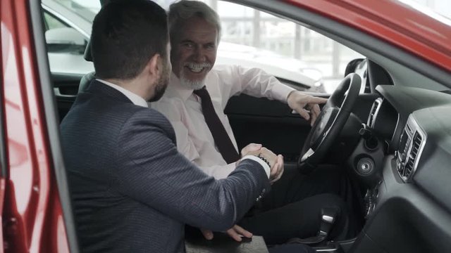 Young professional sales man, is showing a car to a potential customer in the salon. Looking representive. Suit and tie.