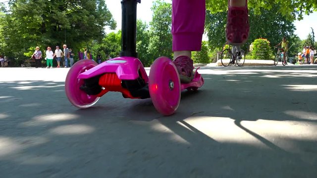 Little child learning to ride a scooter in a city park, feet view