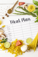 A meal plan for a week on a white table among products for cooking - pastas, basil, vegetables,...