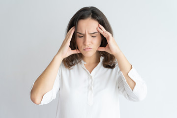 Frustrated tired girl suffering from headache. Young Caucasian woman in white blouse touching head...