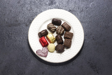wooden red heart with various chocolate on white plate for valentine's day, love chocolate concept
