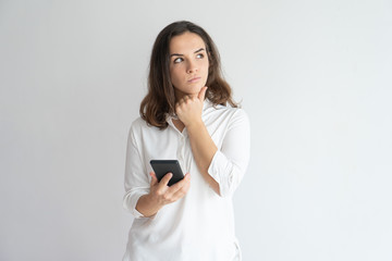 Fototapeta premium Pensive girl thinking over text message. Young Caucasian woman holding smartphone, leaning chin on hand and looking away. Reflecting and communication concept