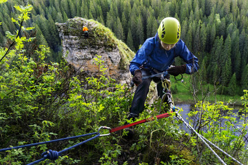 climber girl checks the safety equipment while preparing to descend from the cliff above the river