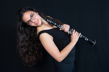 A teenage girl laughing and holding her clarinet music instrument isolated against a black background in the vertical format with copy space.