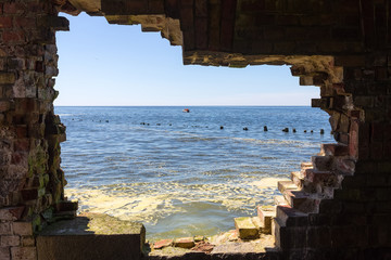 Giant hole in the brick wall of the ancient fortress. View to the azure Baltic sea