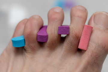 Nahaufnahme eines Fußes dessen Zehen mit Zehentrennern bei der Pediküre getrennt sind fertig zum lackieren