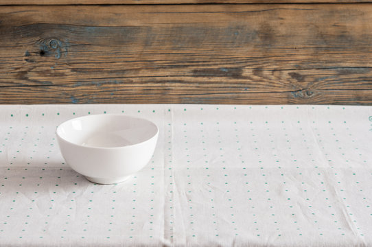 Empty round white bowl with napkin on wooden table