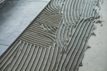 Dark grey ceramic floor tiles laid on applied adhesive