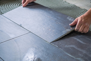 Worker`s hands placing ceramic floor tile with precision on adhesive surface