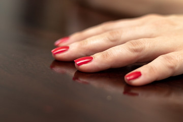 Close up of a girls hand with red coated nails on a dark wooden table