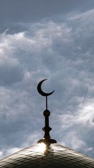 The symbol of Islam is a golden crescent moon on top of the mosque minaret on the blue evening of the morning sky with clouds. Vertical shot.