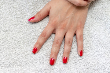 Womans hand with red finger nails lying on a white towel 